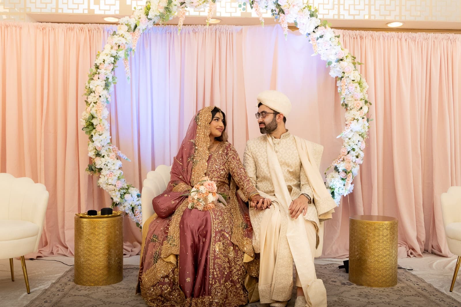 Cover: Ayesha and Faisal seated inside a circular floral arch against a blush pink backdrop