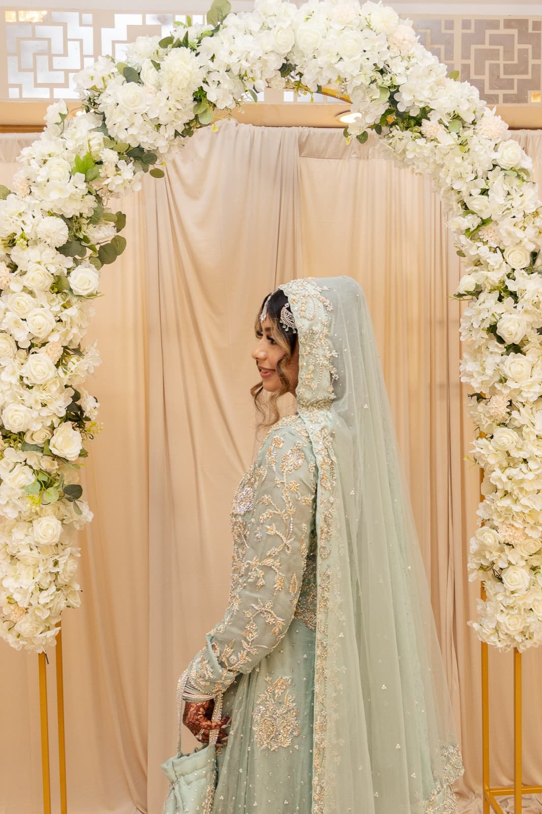 Walima day: Ayesha in mint and silver glancing back under the white floral arch