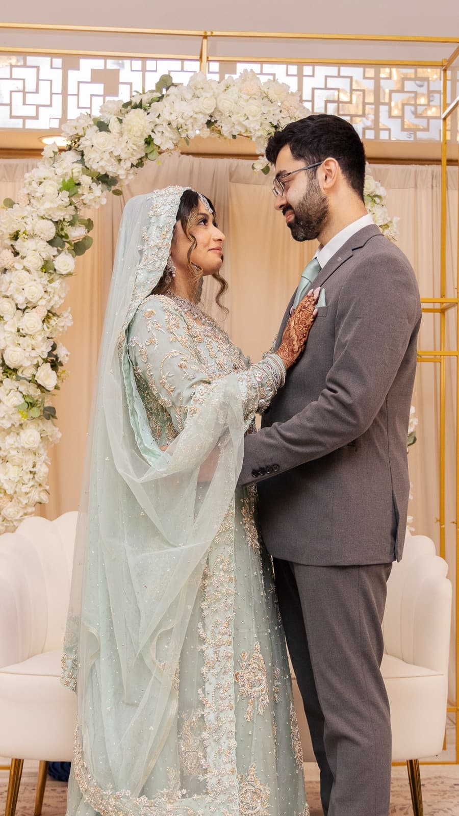 Face to face at the walima, mint gown and grey suit against the white florals