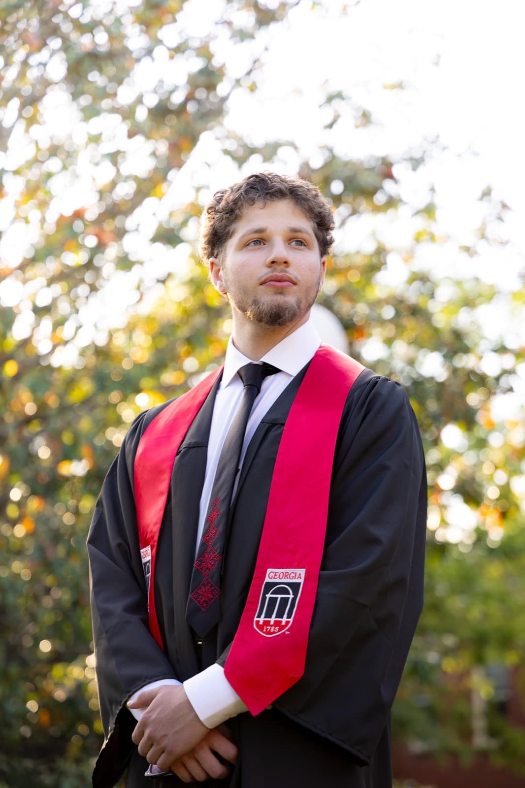 Golden-hour portrait under the trees, red stole and tassel